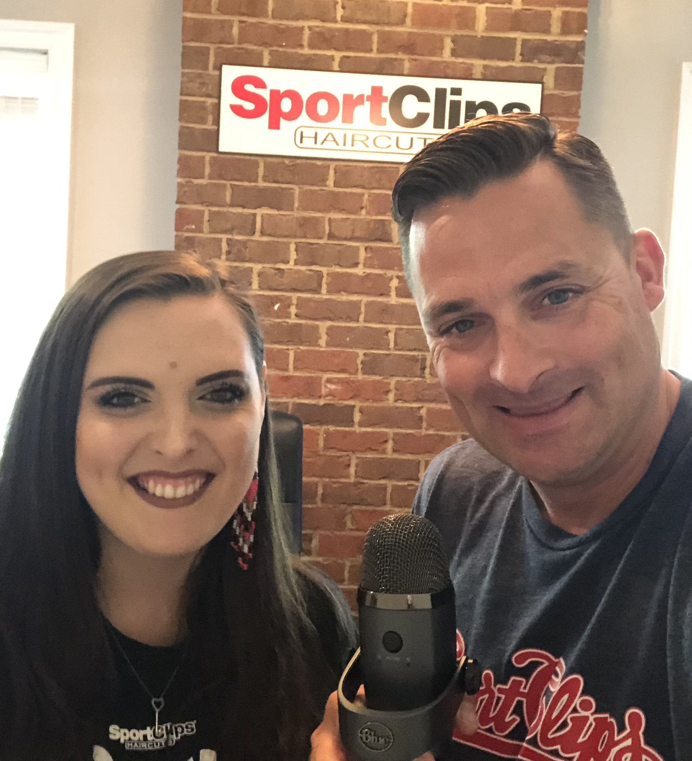 Chad Jordan and Katie Hackney holding a microphone in front of a Sport Clips sign